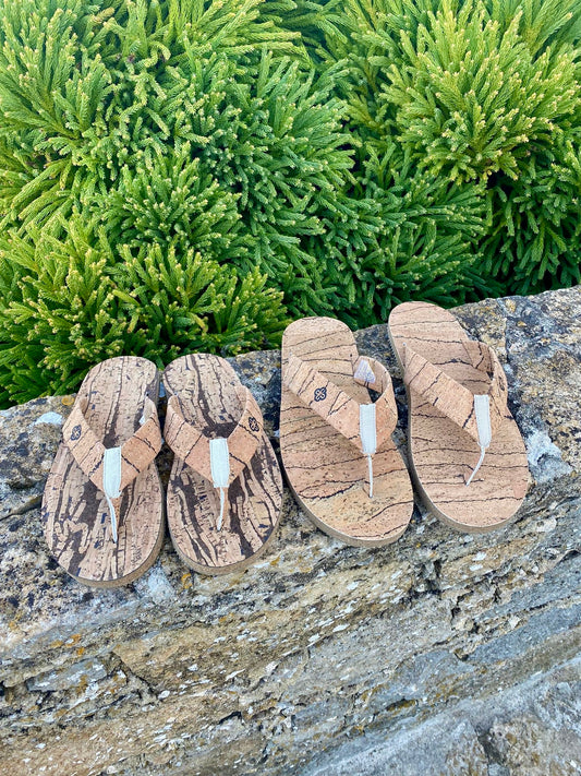 top view of Two Pair of natural cork flip flops on stone wall in front of green bush