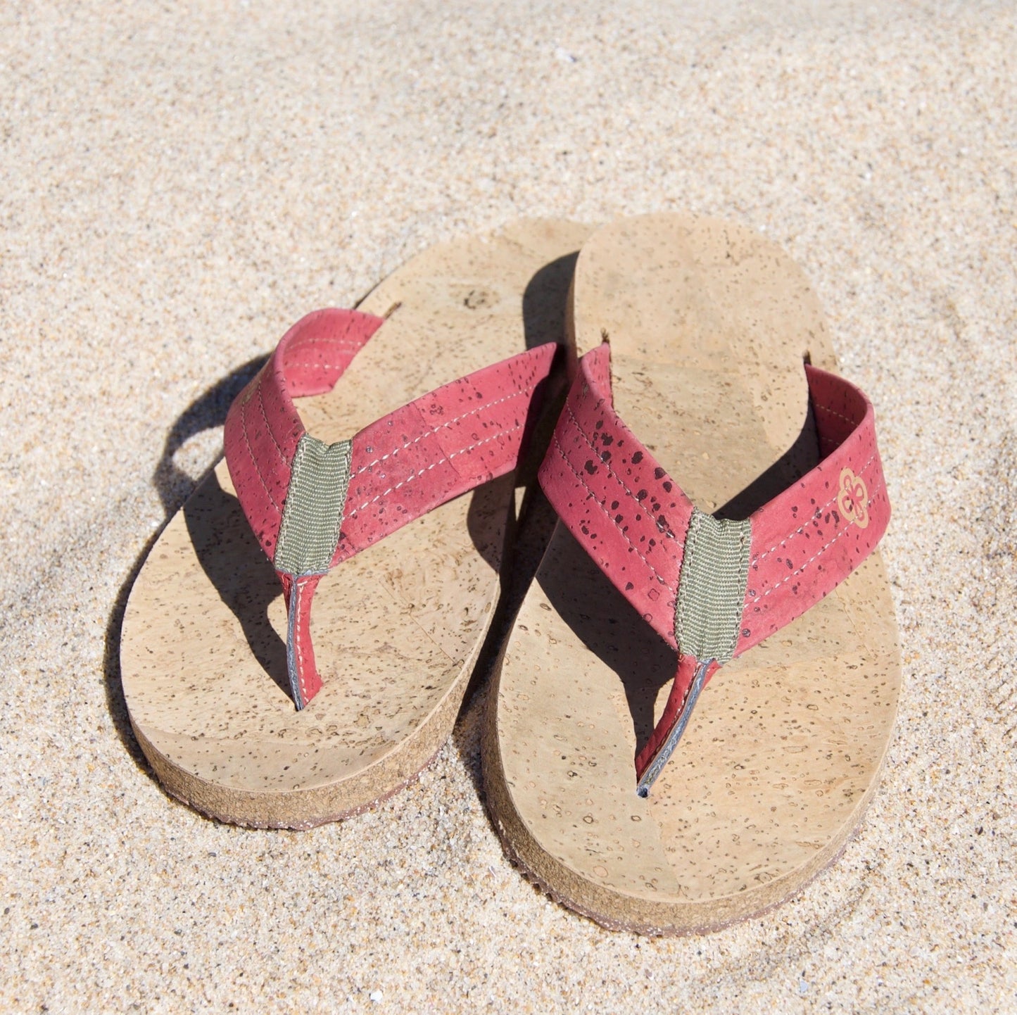 red and beige cork flip flops on sand