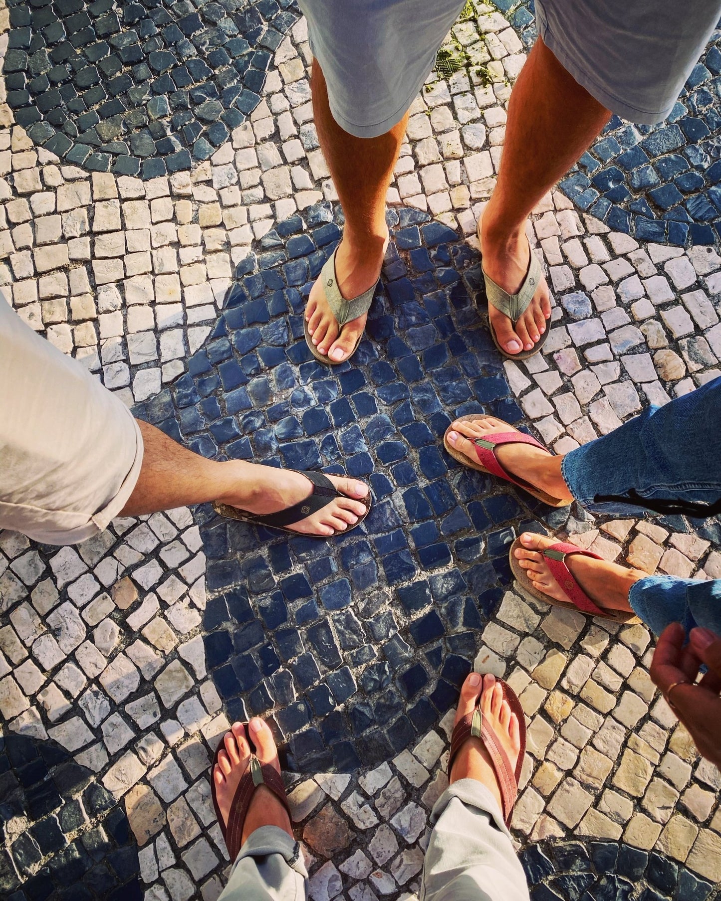 four pair of different color flip flops worn by feet on cobble stone floor