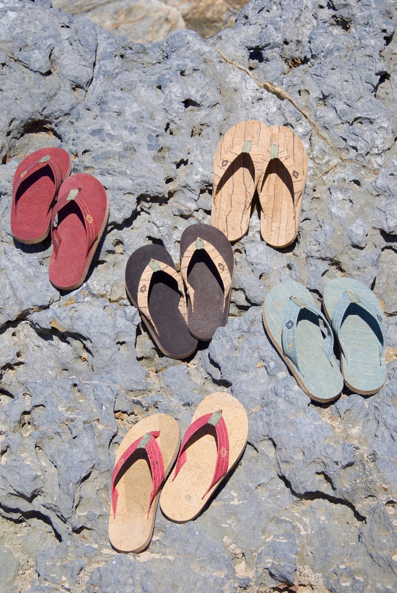 five pairs of different color flip flops on rock