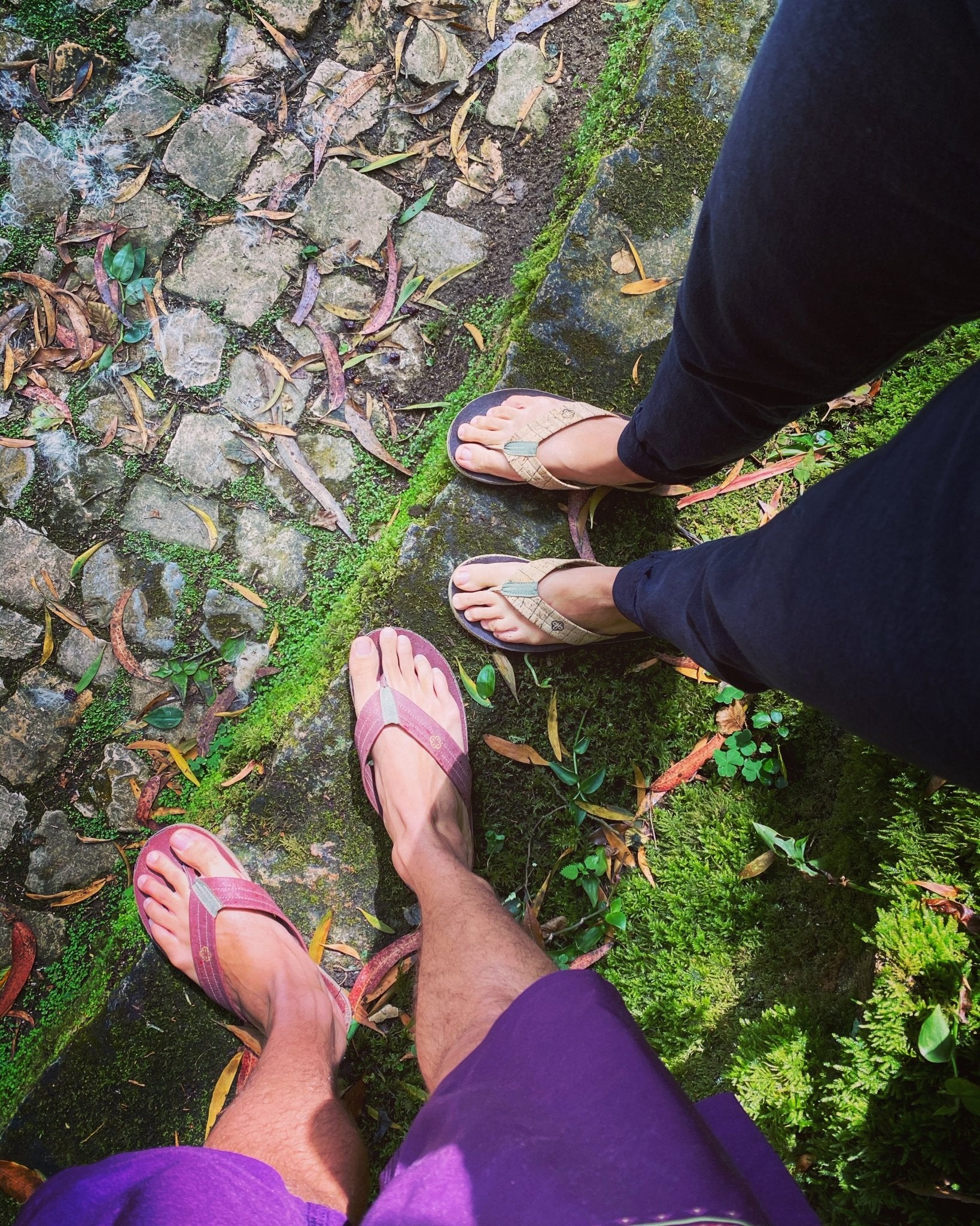 two pair of cork flip flops worn by feet on forest ground